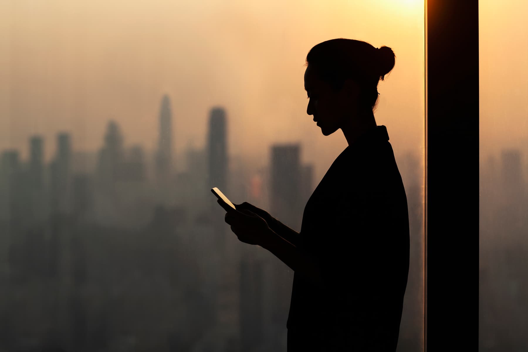 Woman using a phone stands against a background of skyscrapers