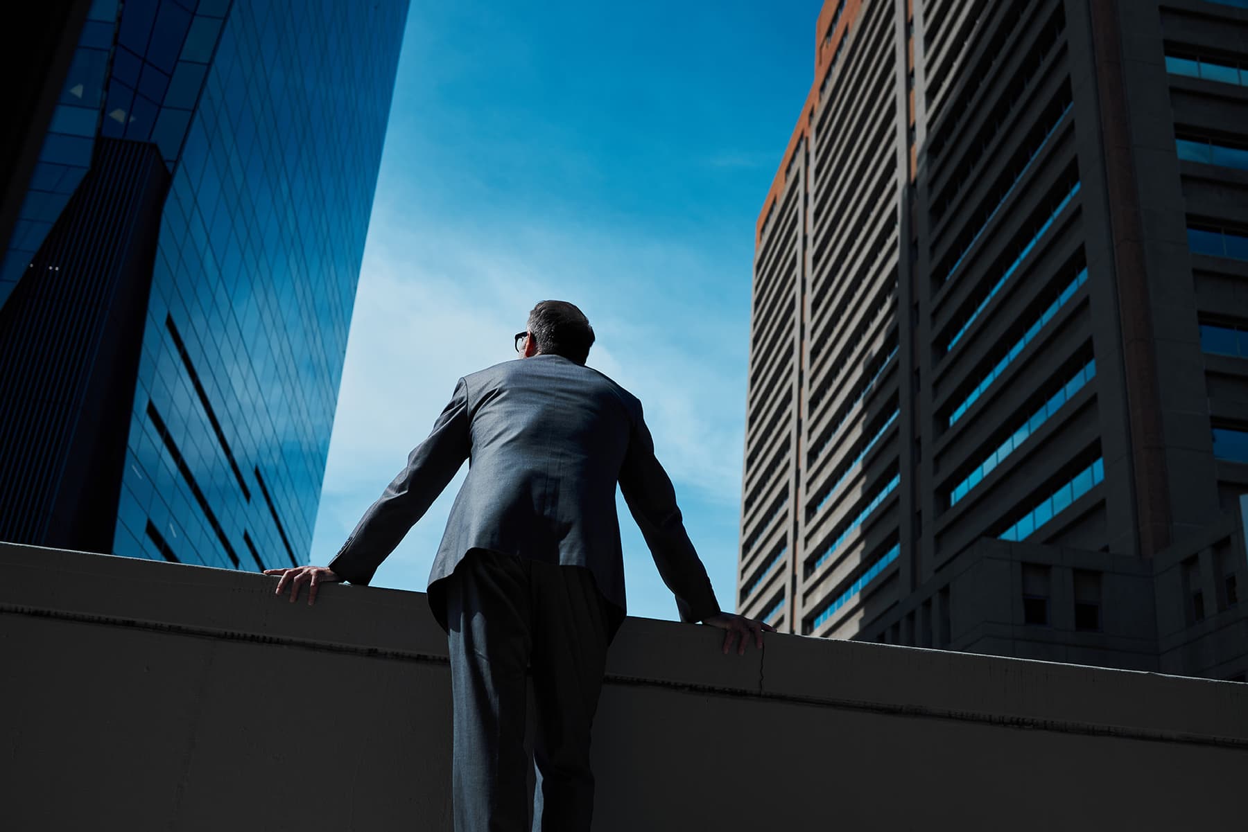 male executive framed by two skyscrapers looking up at blue sky