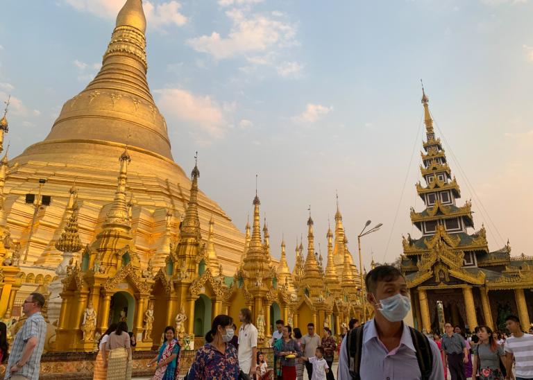 People at Shwedagon Pagoda. Man with face mask on during a global corona virus pandemic.