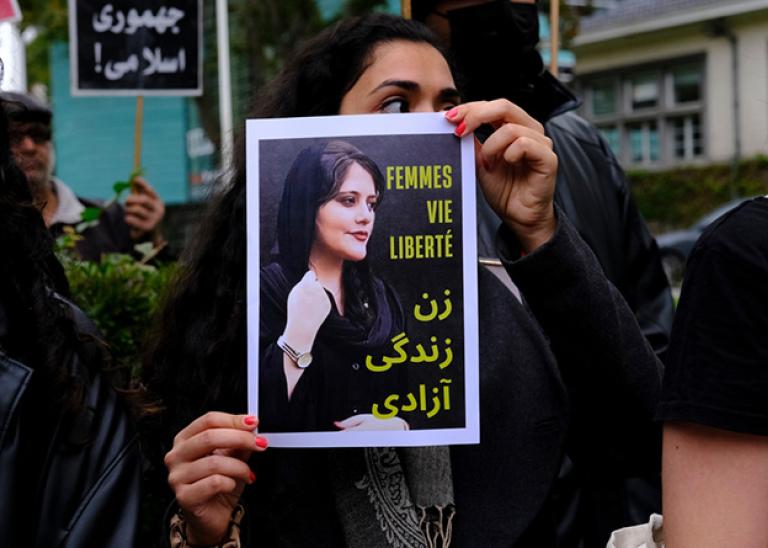 Iranian woman holding up a picture of Mahsa Amini at a public demonstration.